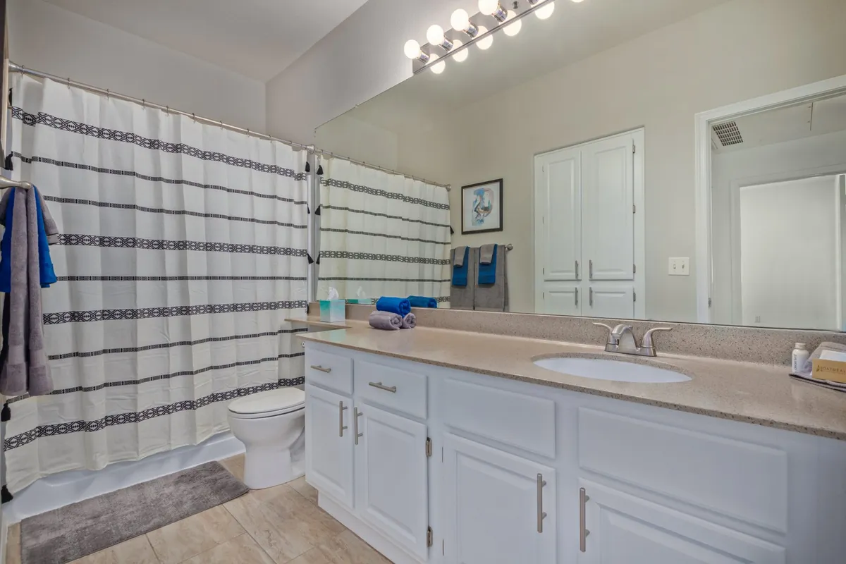 A modern bathroom with a clean vanity, large mirror, shower curtain, and neatly folded towels. The space is organized and well-lit, evoking a spa-like freshness ideal for morning routines.
