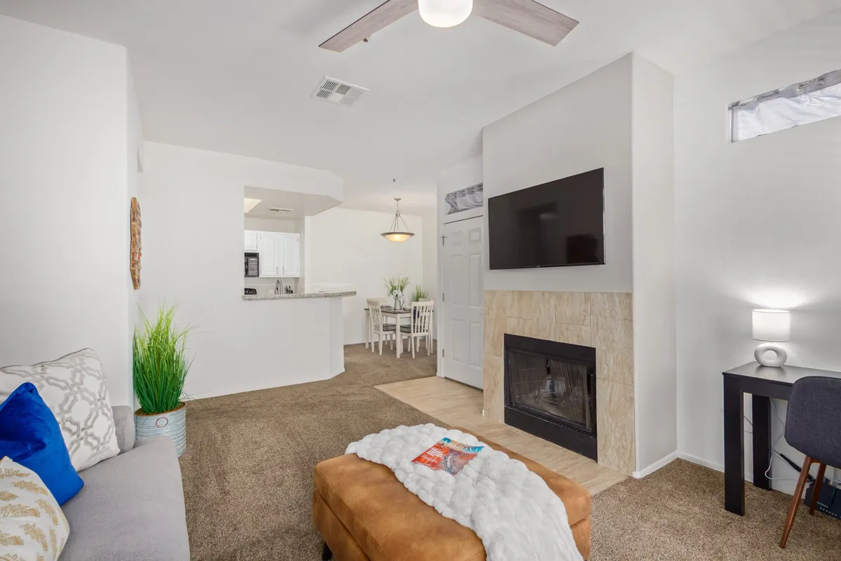 A warm living room scene featuring a plush sofa, fireplace, and thoughtfully placed decorative elements. The dining area is visible, adding to the open and multifunctional feel of the space. The ambiance is cozy and perfect for relaxing or social gatherings.