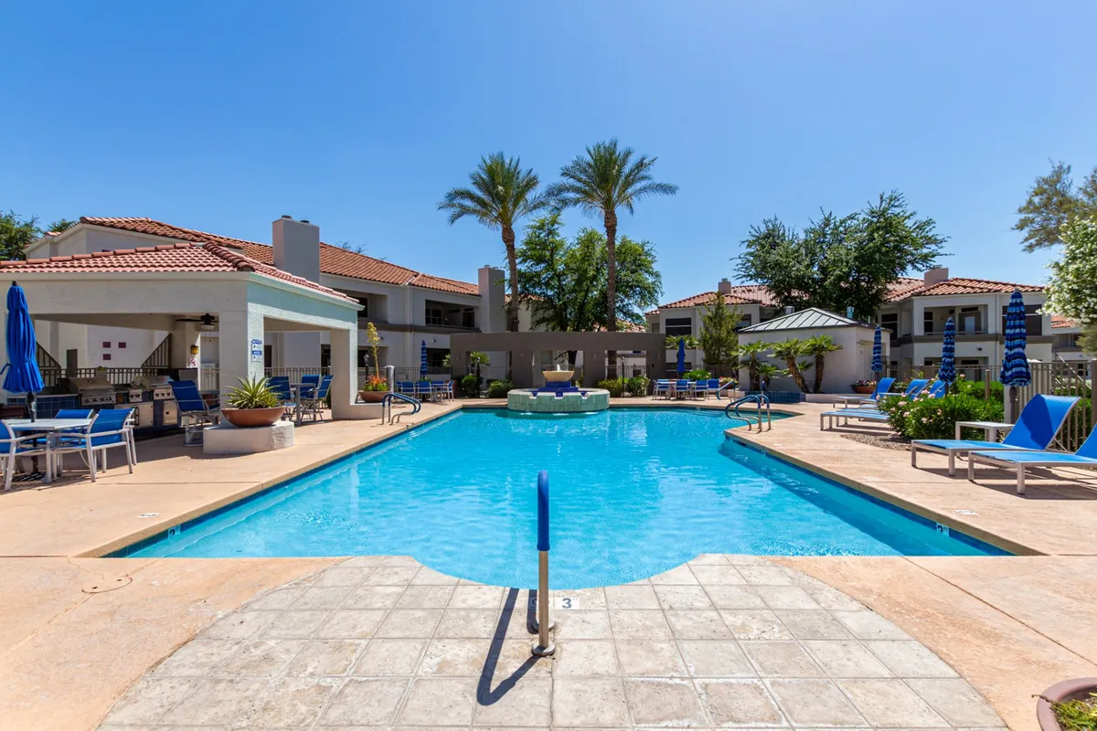 This image captures the sparkling oasis-style heated swimming pool surrounded by lush palm trees, stylish sun loungers, and a barbecue area. The scene is lively yet peaceful, highlighting the opportunity for guests to relax, swim, or socialize in a resort-like setting.