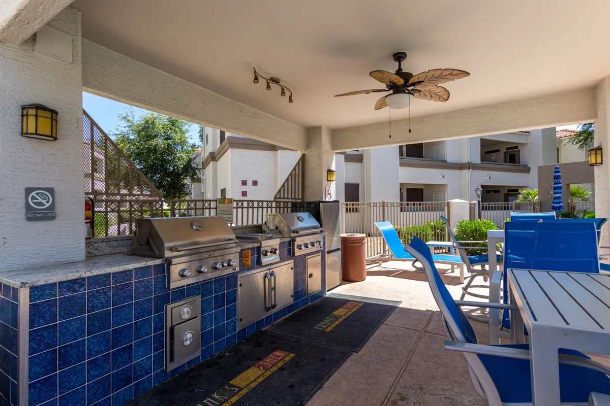 An inviting outdoor dining area with blue chairs and grill stations, set in a landscaped communal space. The setup encourages outdoor meals, casual relaxation, and social gatherings in a comfortable environment.