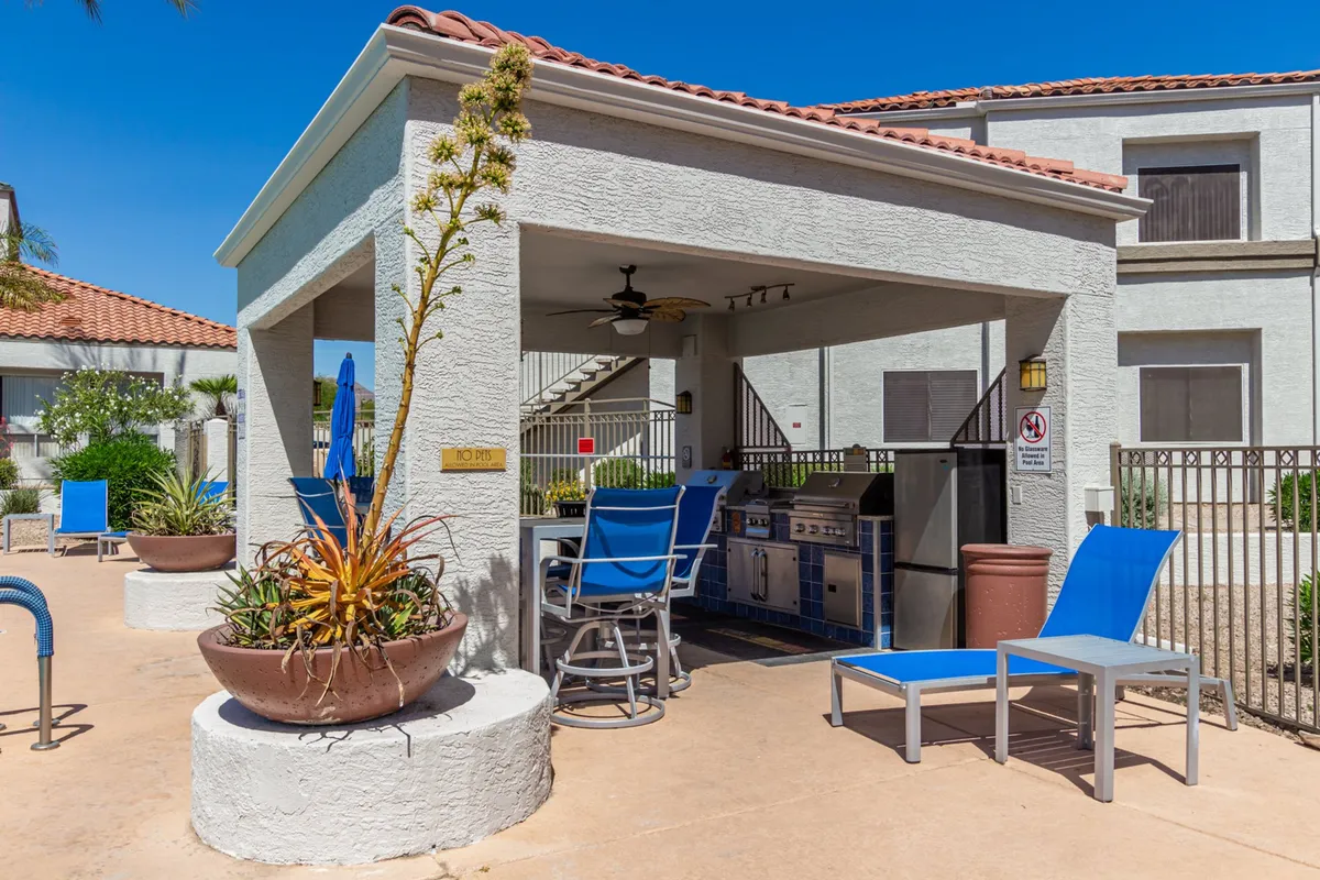 An outdoor kitchen and barbecue grill paired with a comfortable seating area and lush potted plants. The space invites outdoor dining, socializing, and relaxation in a casual, stylish setting.