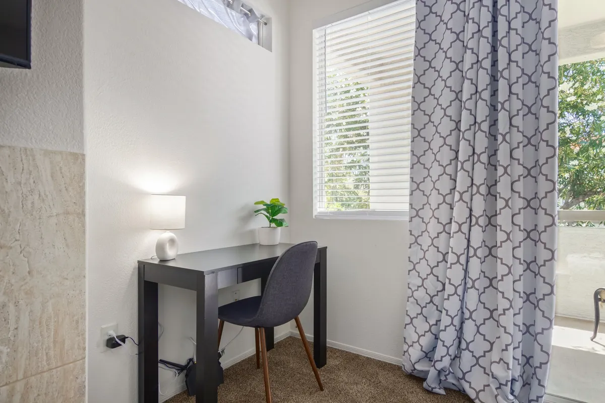A bright, functional workspace with a desk, chair, lamp, and window with curtains. The setup is designed for productivity, allowing guests to work or study efficiently with natural light and peaceful surroundings.
