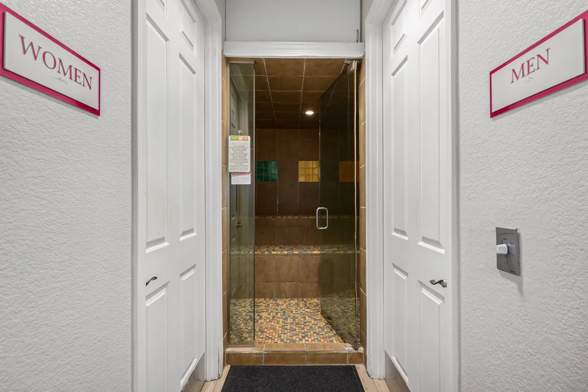 The image shows a brightly lit and functional shower area, marked with men's and women's signage and featuring a colorful tiled floor. The welcoming design suggests a space for refreshing after a workout or busy work session.