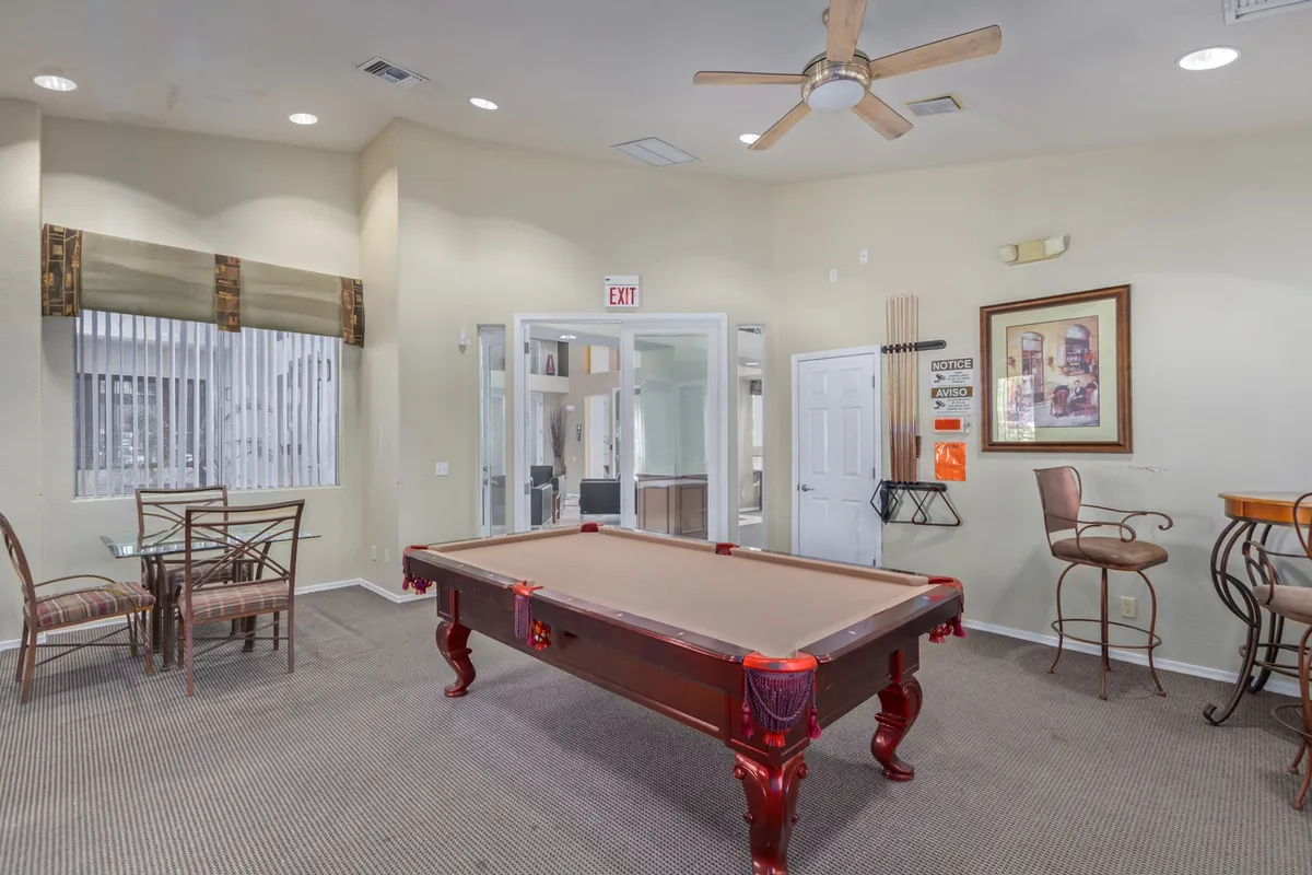 A spacious game room with a pool table and a relaxed seating area, opening up to another room through wide doors. The setting feels casual and sociable, ideal for winding down or enjoying friendly interactions.