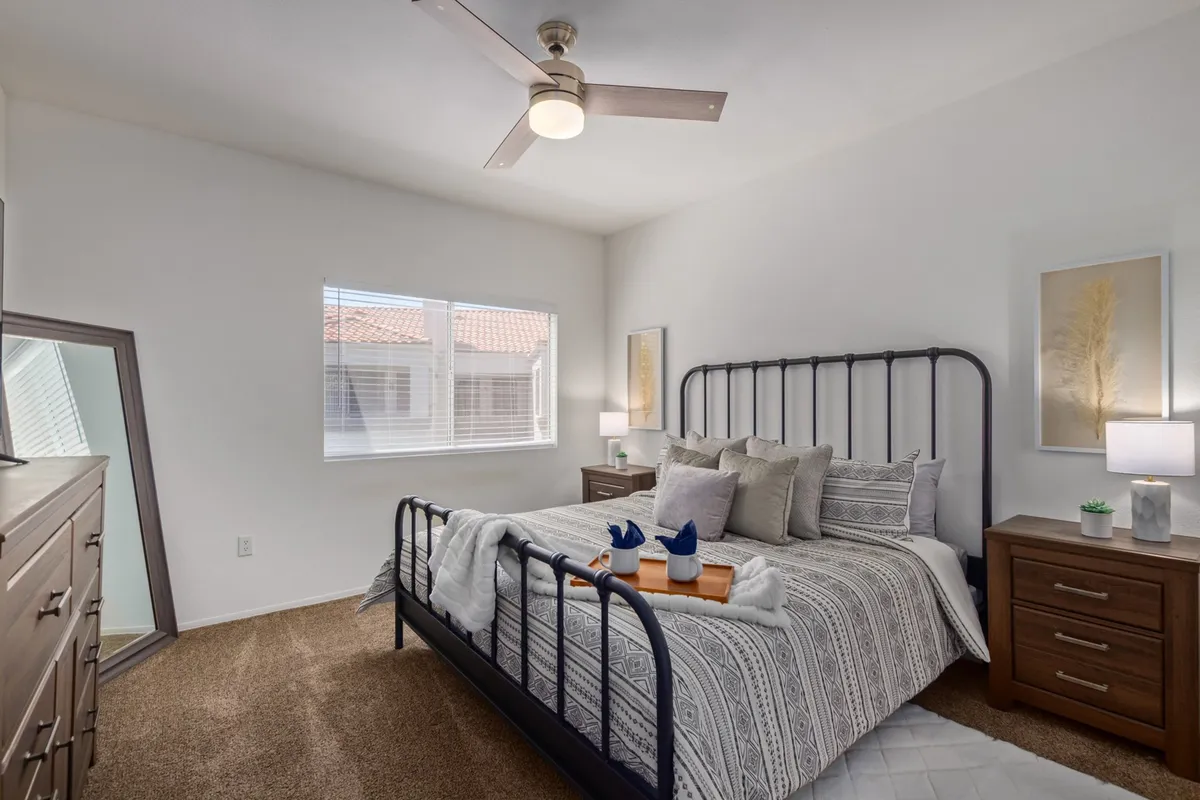 A serene bedroom featuring a neatly made bed with decorative pillows, matching nightstands with lamps on either side, and a mirrored dresser. Soft natural light fills the room, creating a tranquil and restful ambiance.