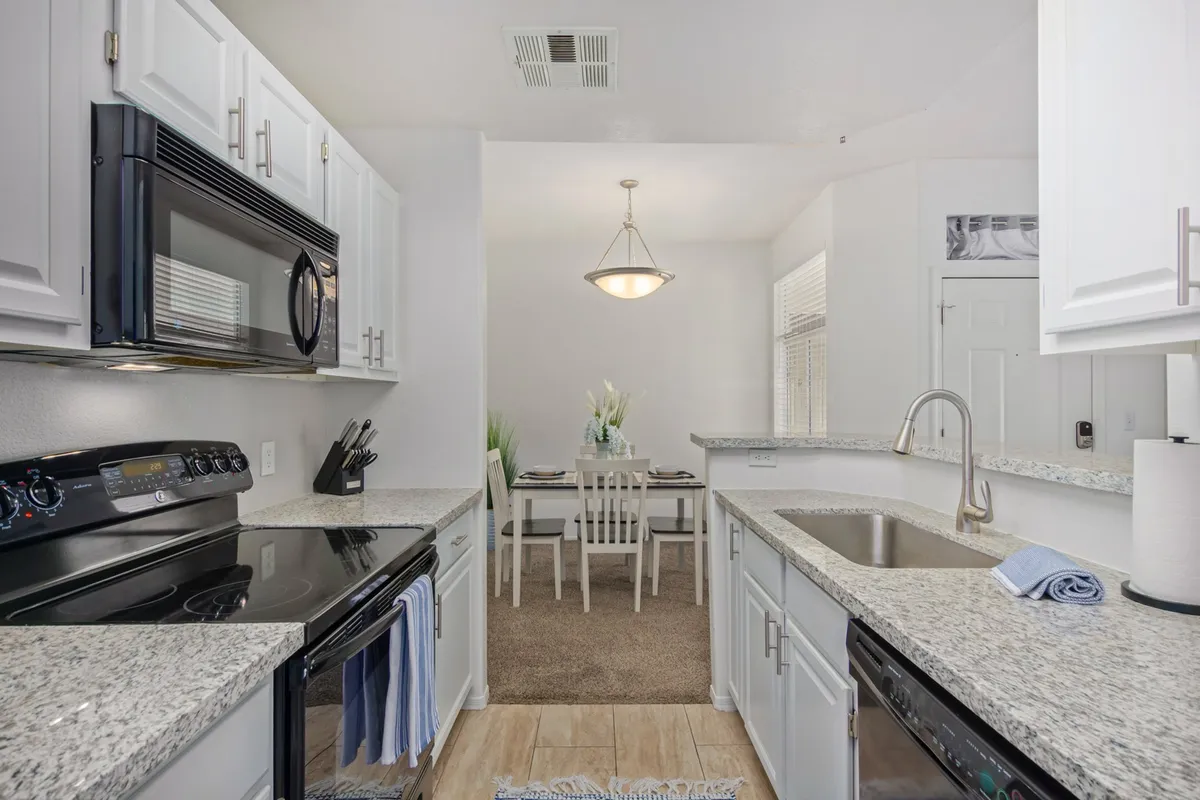 This image captures a cheerful and welcoming kitchen scene, showcasing modern kitchen appliances, granite countertops, and a view of the adjacent dining area. The space is bright and inviting, with plenty of room for meal preparation and social interaction.